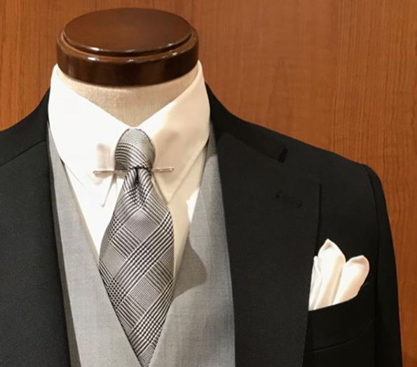 ブラックスーツにライトグレーのベスト（ジレ）、白無地のシャツ、グレナカートチェックのネクタイ、シルバーのカラーピン、白のシルクのチーフ