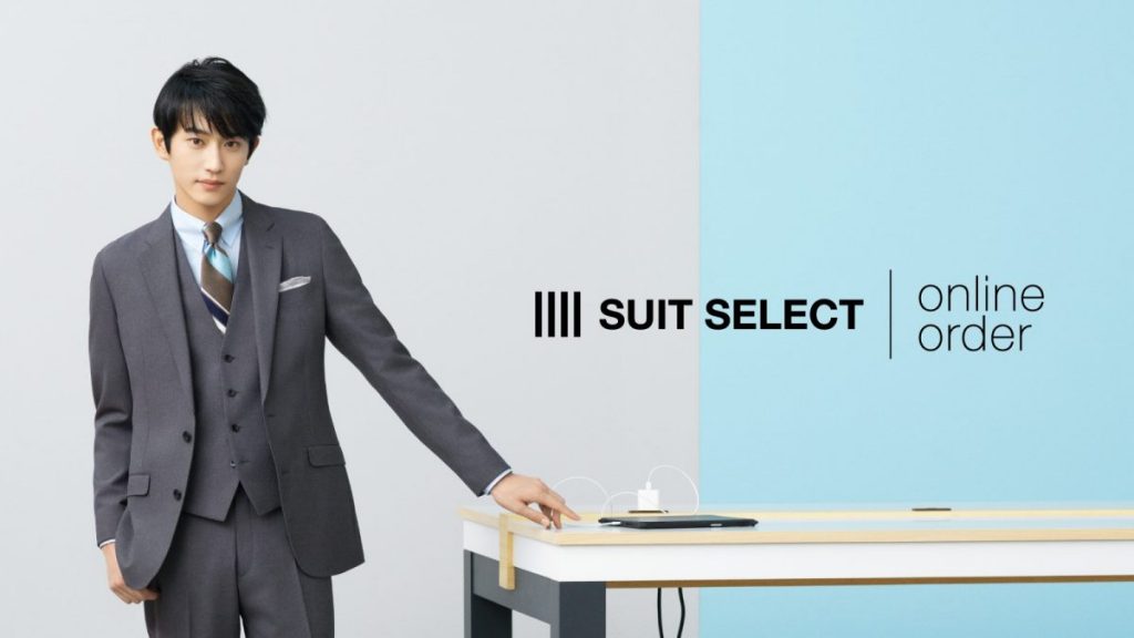 AI SPEED ORDERの画像。俳優の杉野遥亮さんがグレーのスーツとレジタルタイを着用。
バックのカラーは、左半分強がグレー、右側が水色。左側に杉野さんが立って、左手を左側に位置している机に軽く触れている。